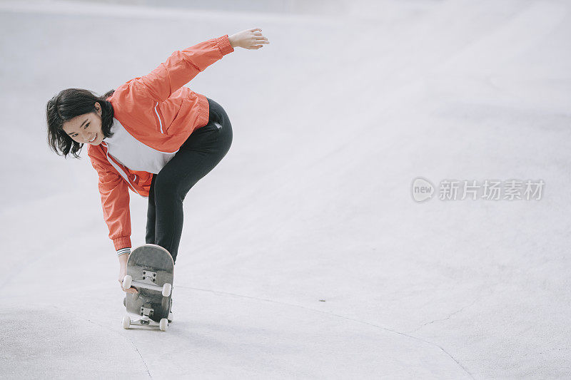 一个年轻的中国女孩周末在公共滑板公园练习滑板