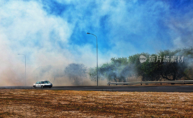 汽车在野火的浓烟中行驶，旁边的草因干旱而干枯