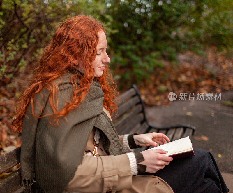 一个十几岁的女孩坐在公园的长椅上，平静地读着一本书