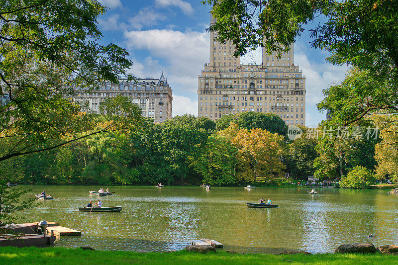 纽约曼哈顿，中央公园的湖，人们享受划艇，秋色的树木和背景中的圣雷莫合作大楼。