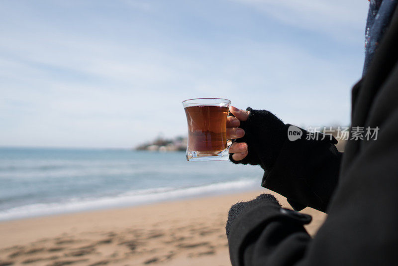 在海滩上拿着一杯茶的女士。