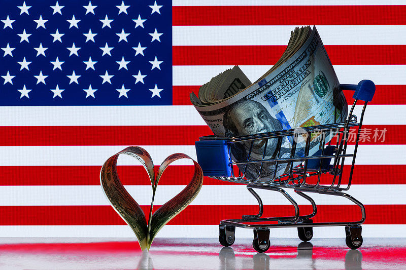 迷你超市购物车里的一叠100美元钞票，旁边是两张以美国国旗为背景的1美元心形标志