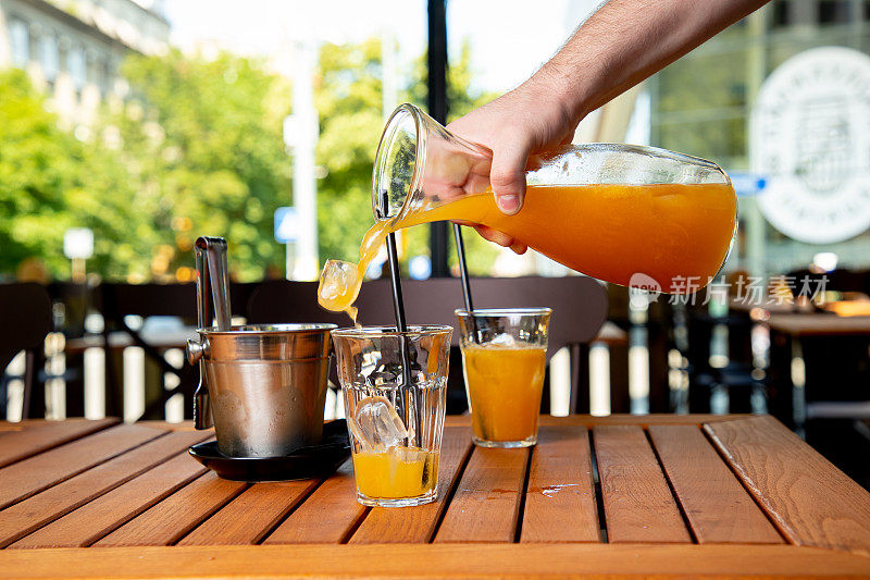 将橙汁从瓶中倒入加冰的玻璃杯中
