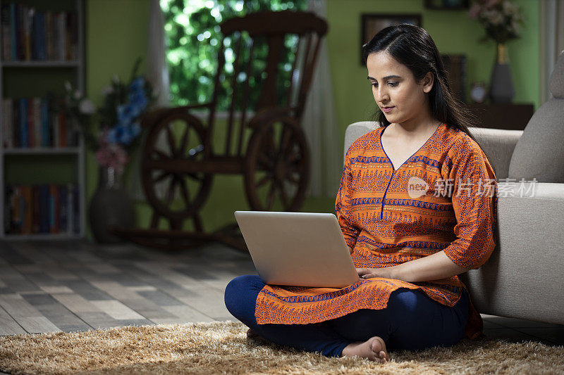 一个年轻女人坐在地板上使用笔记本电脑的肖像:库存照片