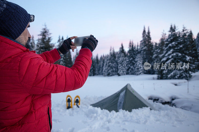 游客在冬季山地露营时在帐篷附近使用手机。在2019冠状病毒病大流行期间，自然是孤独的。心理健康和生活平衡。