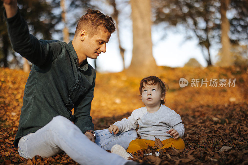 年轻的父亲和他的小儿子在秋叶中玩耍