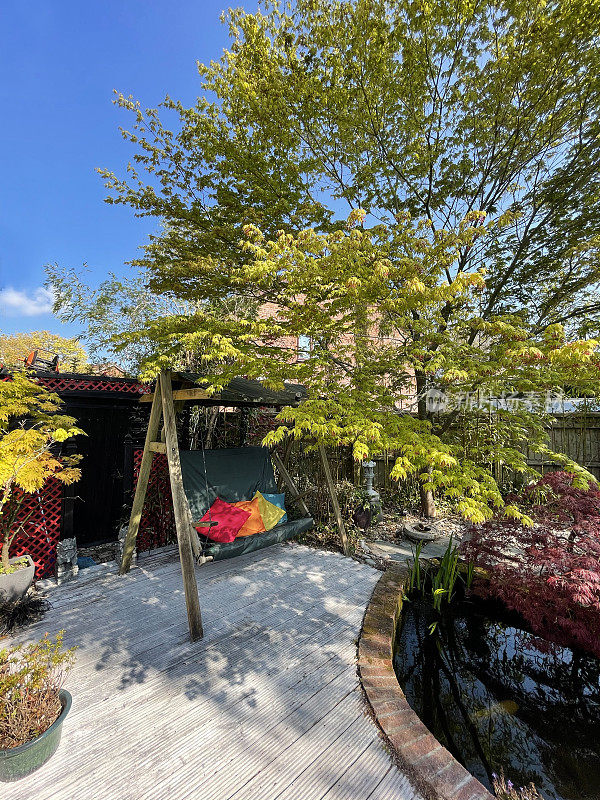 自制的黑色和红色日本茶馆，木制花园秋千椅，具有日本元素花岗岩灯笼，木制甲板，鹅卵石，盆景和日本枫树(槭树)旁边的大锦鲤池塘