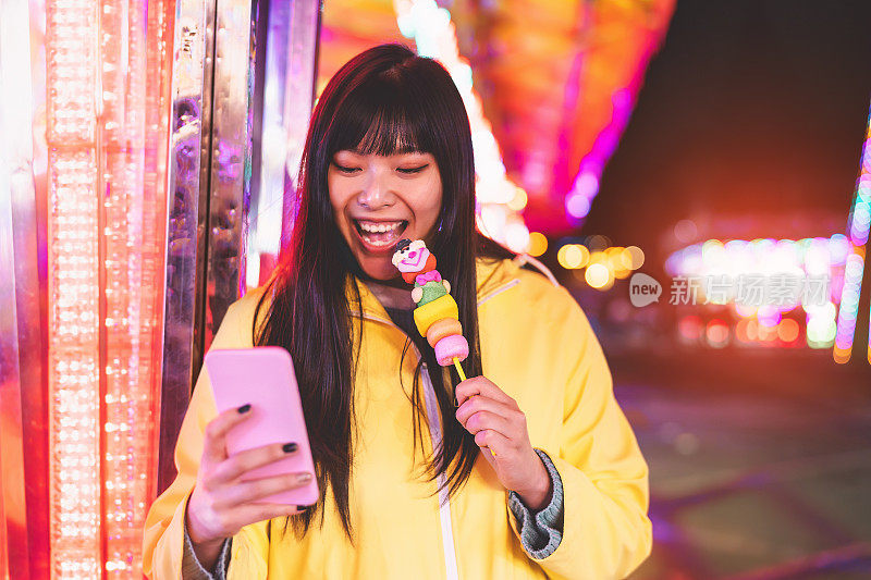 亚洲女孩在游乐园使用手机-快乐的女人享受新的趋势智能手机应用程序-青年一代和社交媒体成瘾的概念