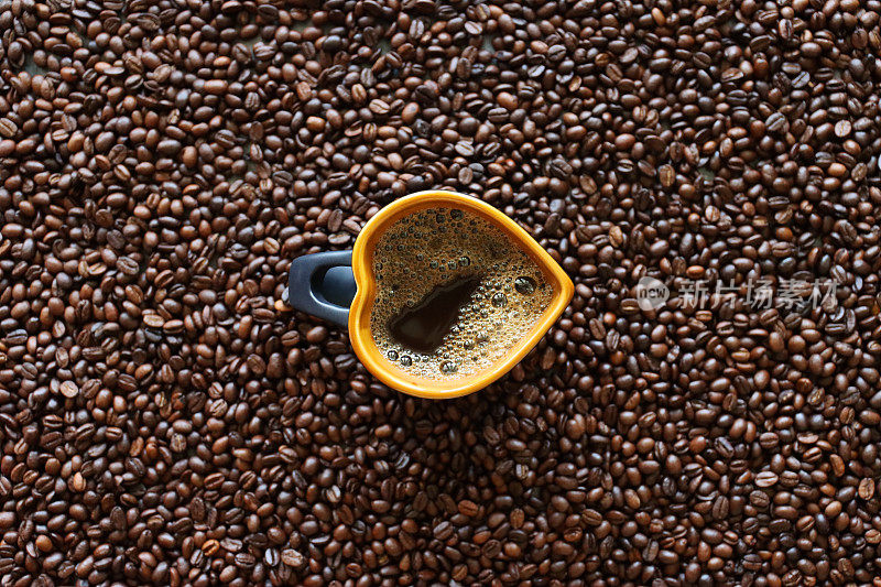 中国的形象，心形的杯子装满了黑咖啡坐在一堆烤咖啡豆的背景，升高的视野
