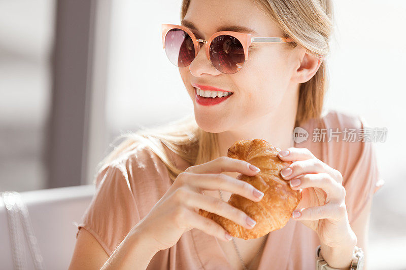 年轻女子坐在咖啡厅，休息时间吃牛角面包