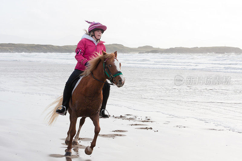 兴奋的女孩和小马享受自由骑在海滩上。