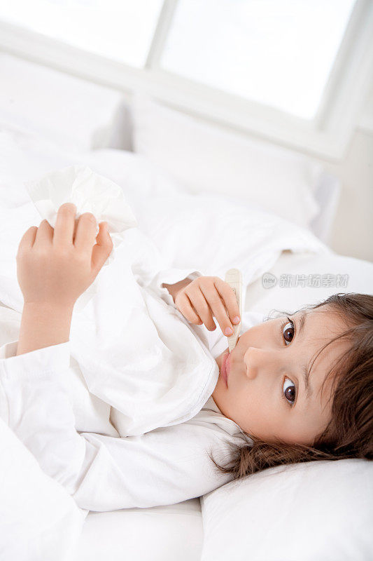 生病的小女孩躺在床上拿着体温计