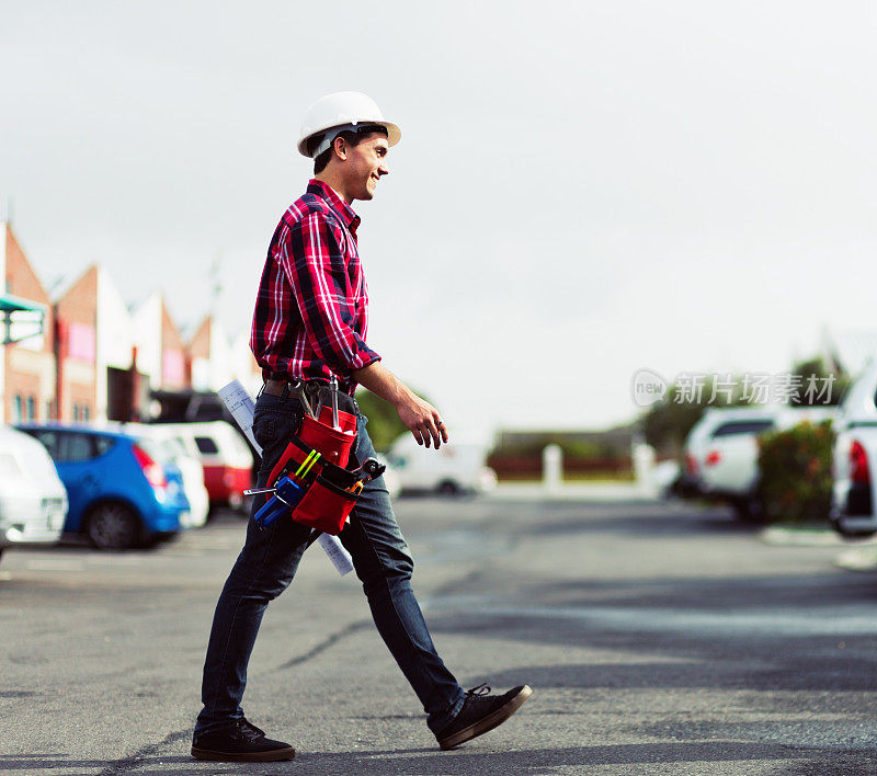 年轻的工人戴着安全帽和工具带穿过马路