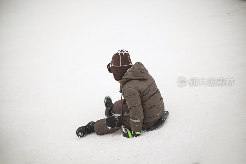小男孩在雪中从山上滑下来