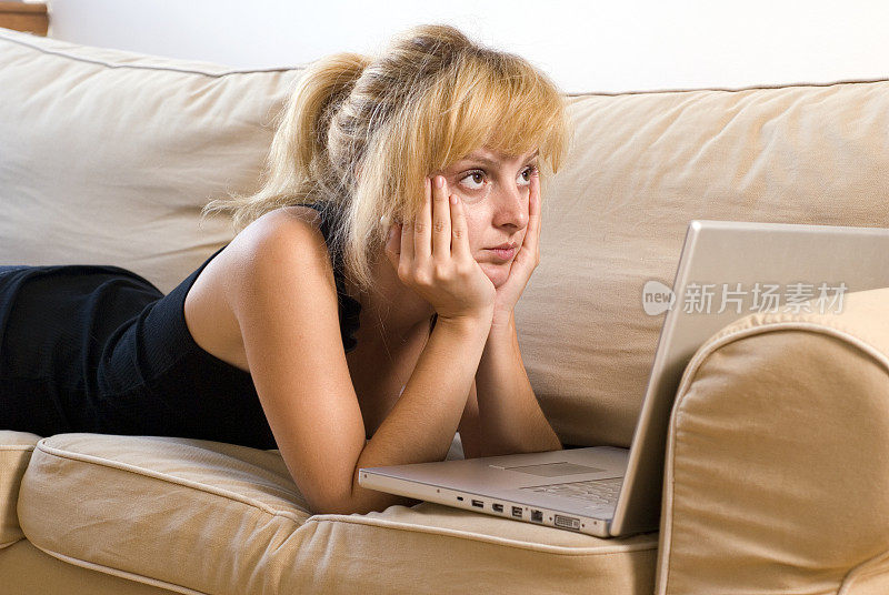 年轻女子躺在沙发上用笔记本电脑