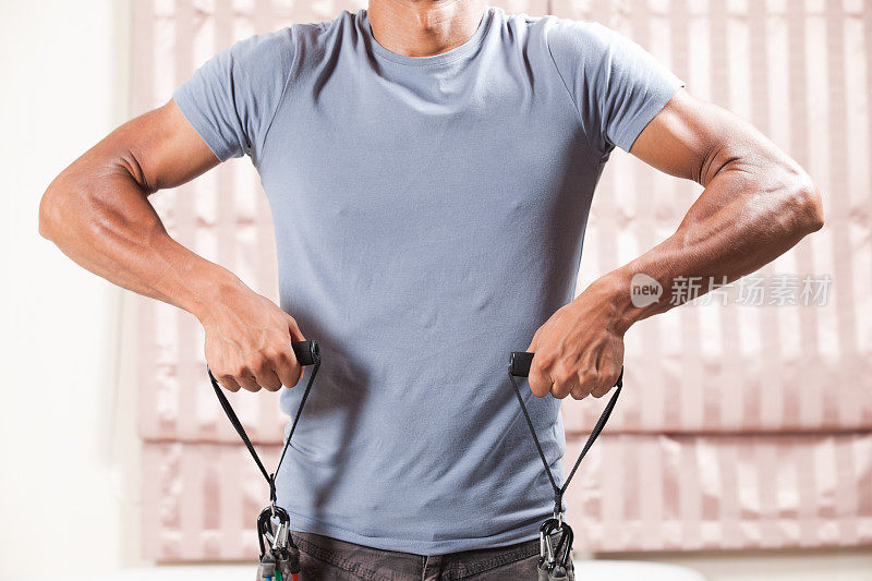 肌肉发达的男性在家里使用阻力带。直立行