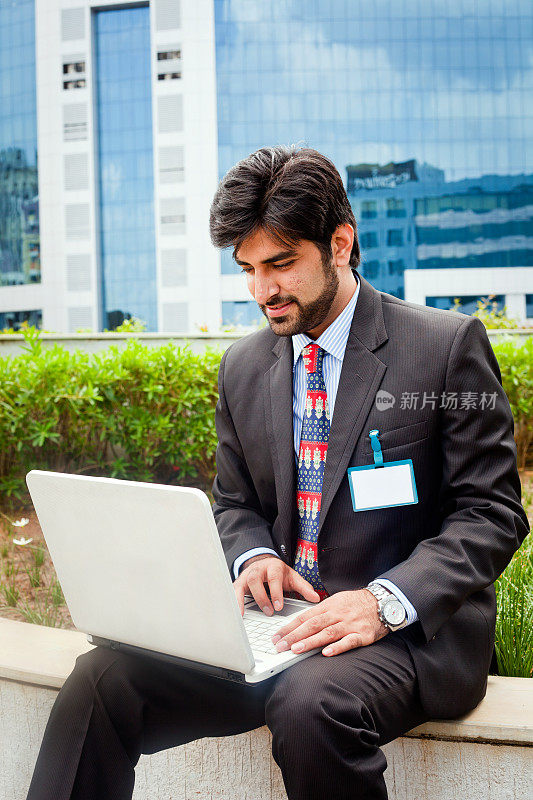 年轻的亚洲印度商人坐在户外使用笔记本电脑