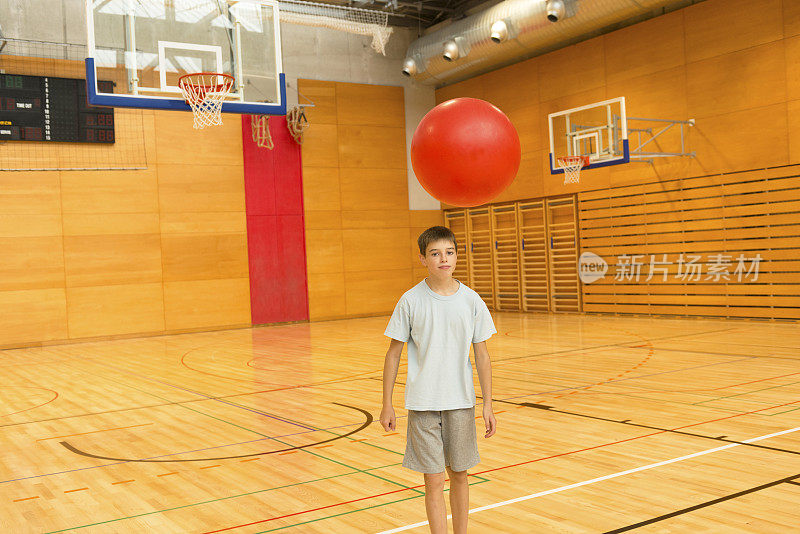 十一岁的男孩在学校体育馆玩红色健身球