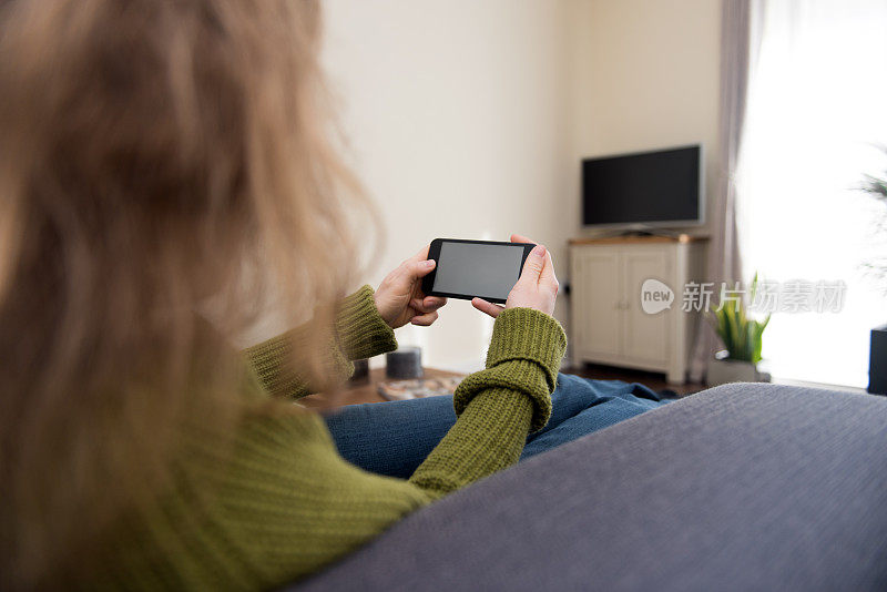 金发女人正坐在家里看着手机屏幕上的技术背景