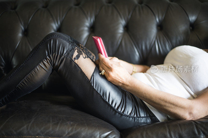 一个女人躺在黑色皮沙发上，拿着一个粉色的手机