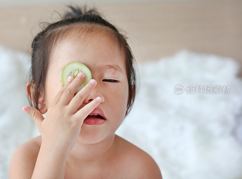 可爱的小女孩拿着黄瓜片在脸上，概念护肤。
