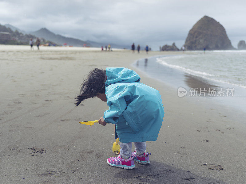 亚洲小女孩在沙滩上玩玩具铲子