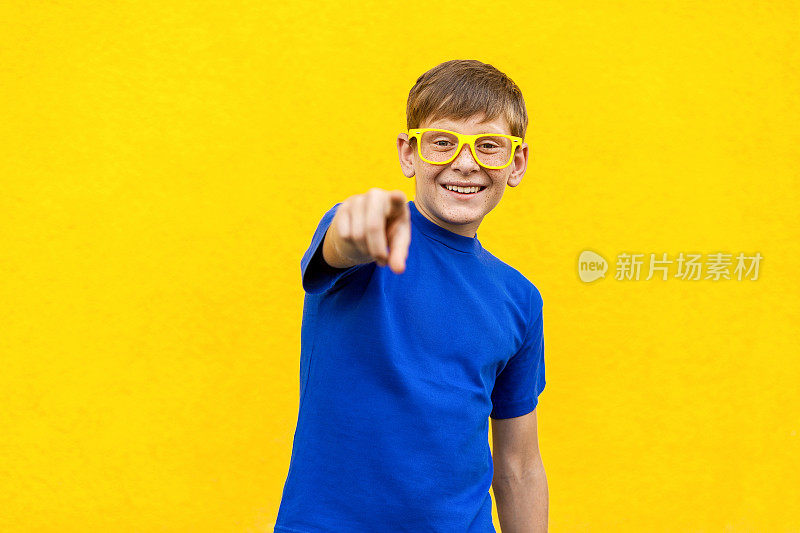 嘿,你!幸福的小男孩戴着黄眼镜，指着手指，看着镜头。