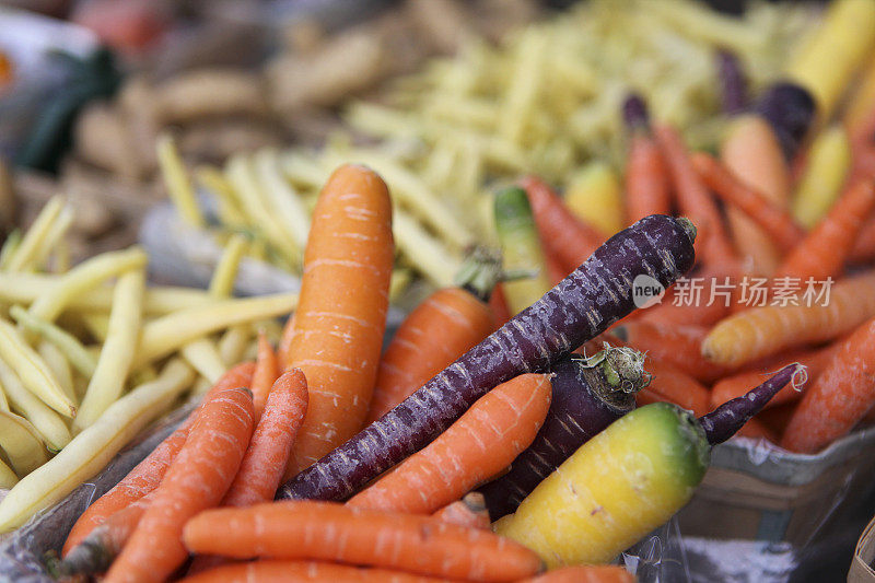 在一个户外的公共市场上，五颜六色的胡萝卜、黄豆和生姜都在出售。