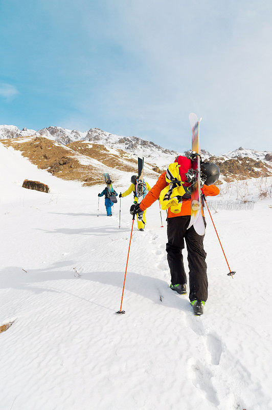 一组三个自由骑手爬上这座山，在荒野的山坡上滑雪