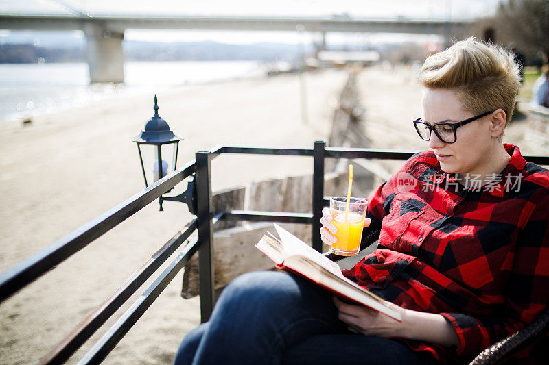 一位美丽的年轻女子坐在河边的咖啡馆里看书
