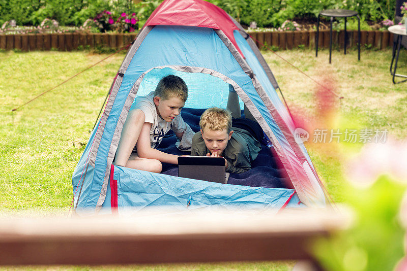 野营时，男孩们坐在帐篷里，在平板电脑上看视频