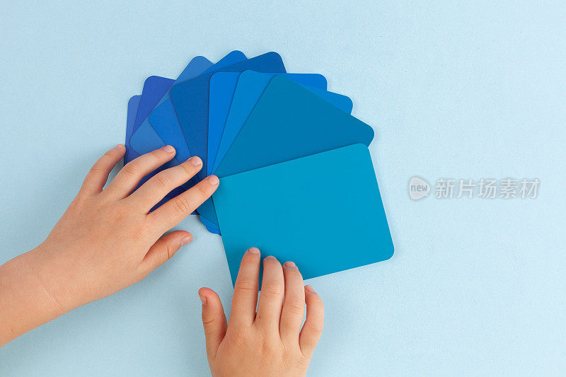 孩子的手玩颜色样本卡-色调的蓝色。顶部视图与复制空间
