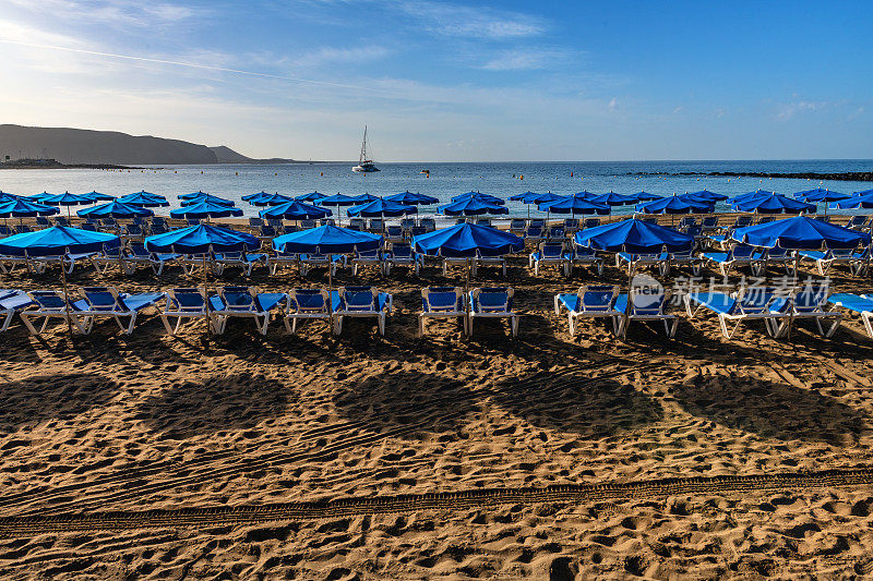 西班牙特内里费岛的洛斯克里斯蒂亚诺斯湾海滩，配有日光浴床和雨伞