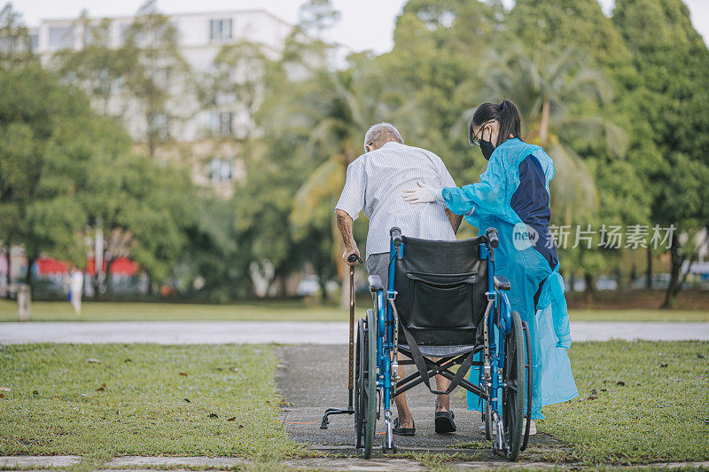 亚洲中国女理疗师帮助老年男子从轮椅上站起来，拄着拐杖在公园里散步