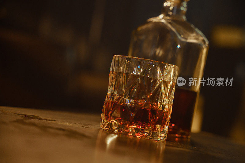 桌子上有一个漂亮的水晶玻璃杯，里面装满了威士忌。威士忌酒瓶半满了。漂亮的酒精暖色照片。
