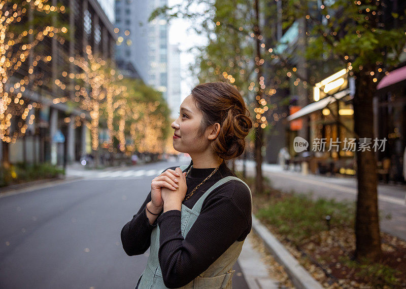 一个年轻的女人站在挂着圣诞彩灯的街上