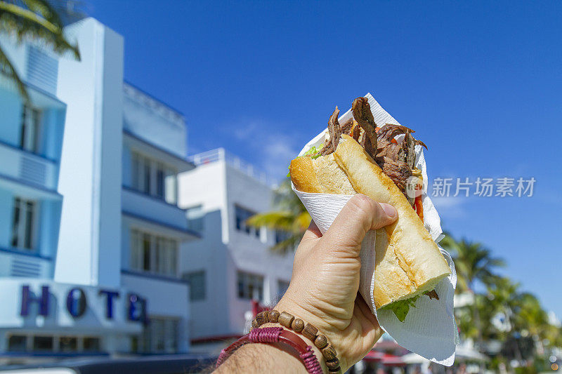 一个年轻的旅行男性享受他的假期，吃着古巴三明治在海洋大道前，南海滩，迈阿密，迈阿密，南佛罗里达，美国。