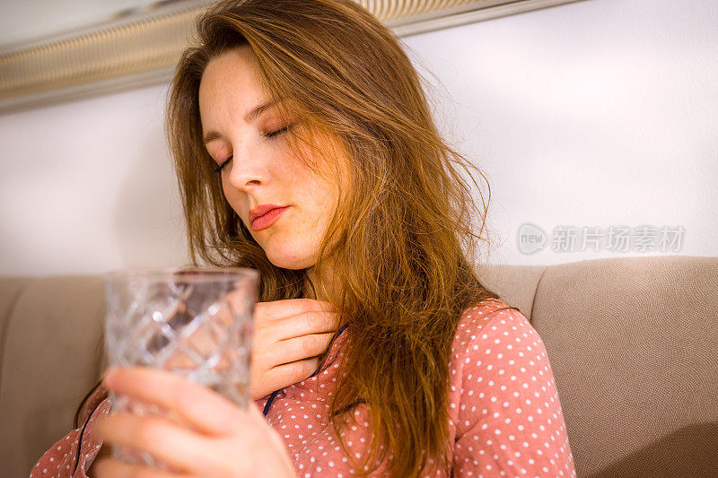 女人坐在床上，摸着喉咙，端着一杯水。