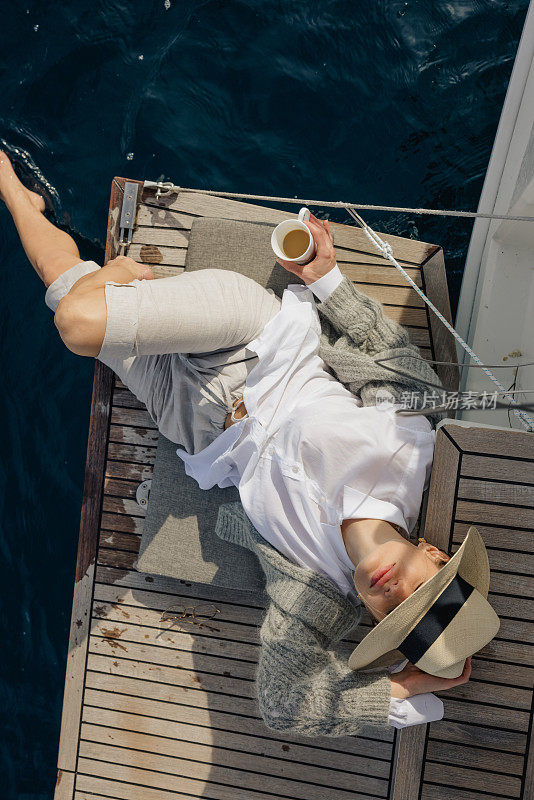 女人们早上在船甲板上放松，手里拿着一杯咖啡，把脚放在水里，抬头看