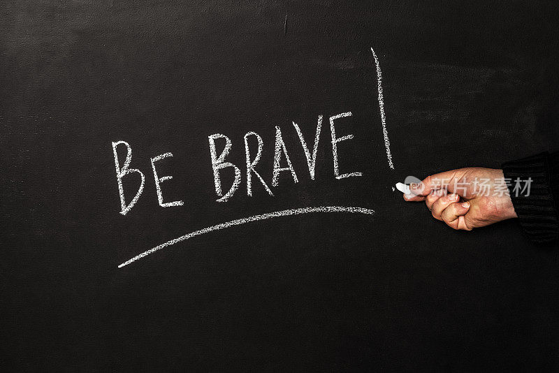 一个男人用白色粉笔在黑板上写下了“勇敢!”