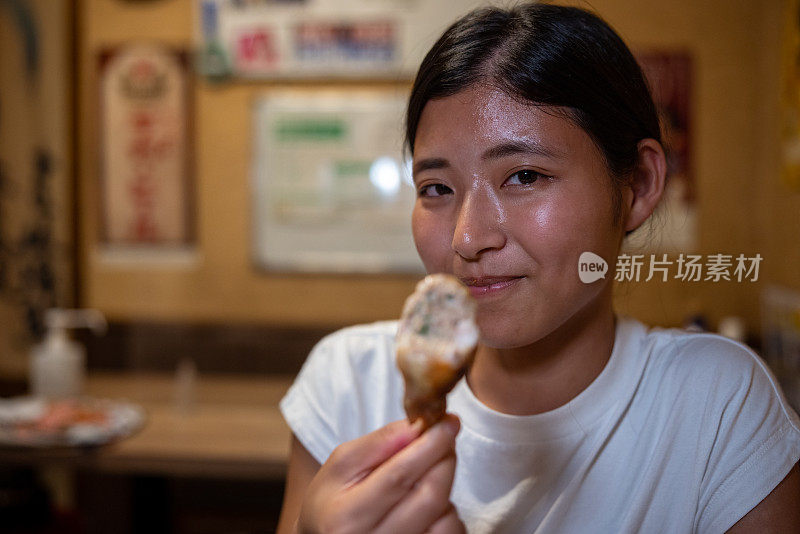 在日本“居酒屋”酒吧，一名年轻女子拿着烤鸡看着镜头