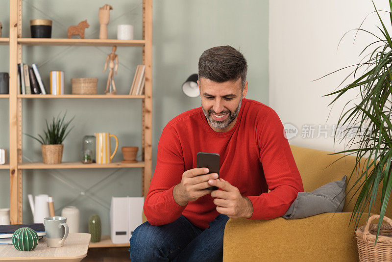 一个快乐的男人在他的智能手机上发短信，在家里享受