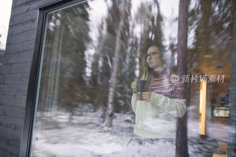 下雪天，一名女子一边喝着热饮，一边欣赏窗外的景色