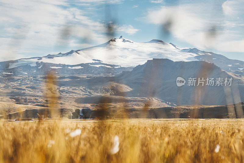 大雪覆盖的冰岛Snaefellsjokull冰川火山山顶，前景中有橙色的草