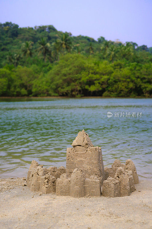 在印度果阿的海滩上建造的复杂沙堡堡垒的图像，用桶和铲子制作，并修改为围绕外部创建一堵墙，背景是大海