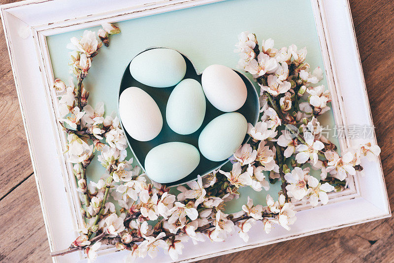 色彩柔和的复古平铺绿色复活节彩蛋在心形盒子与杏仁花枝在质朴的棕色木制背景