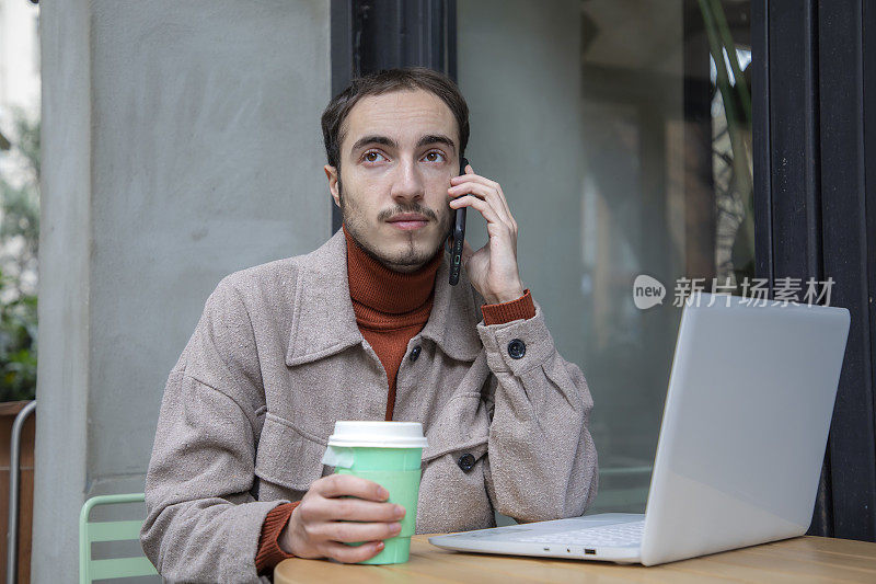 年轻人一边在咖啡馆里打电话，一边喝咖啡，一边用电脑工作