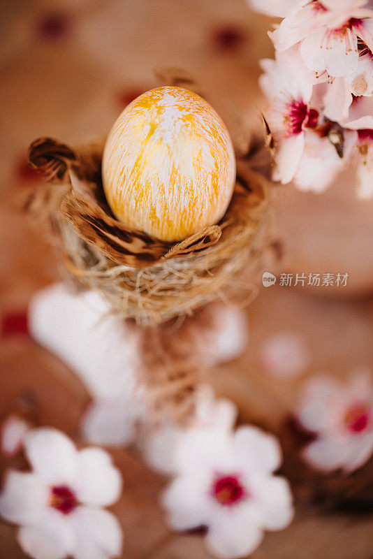 一个金色的复活节彩蛋在一个金色的鸟巢上，在一个白色的柱子上，在一个古老的室外石桌子上，杏仁花