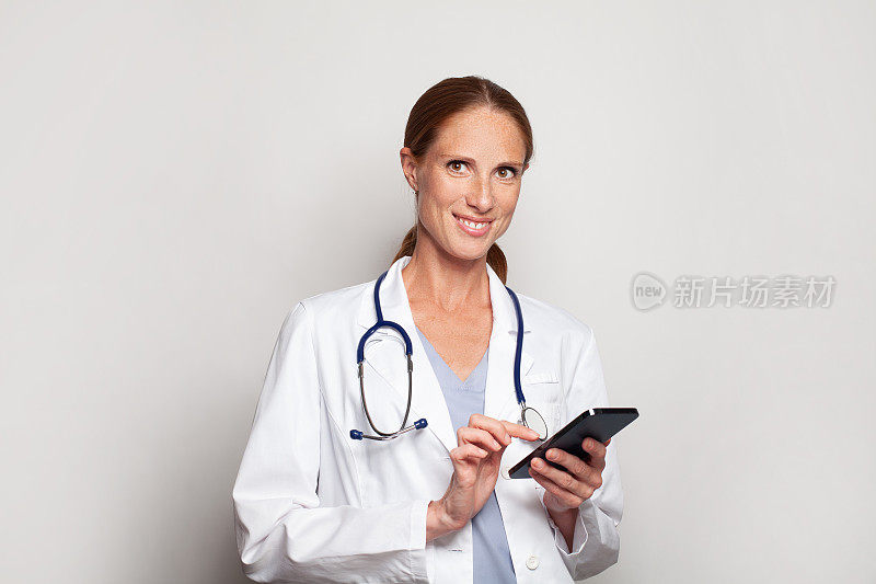 自信微笑的现代中年成年女医生，医务工作者从业人员使用智能手机，女性肖像