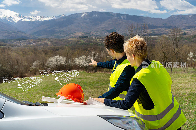 两位工程师在草地上用铅笔画着太阳能电池板，看着山景